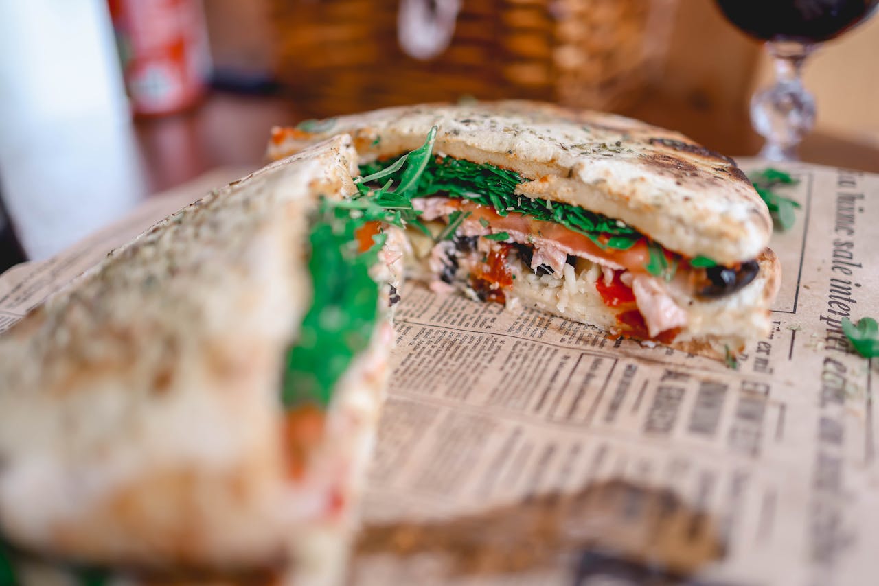 Close-up of a Tuscan schiacciata sandwich with fresh ingredients on a rustic table.