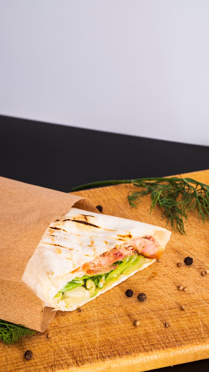 Close-up of a delicious grilled wrap with chicken, lettuce, and spices on a wooden board.