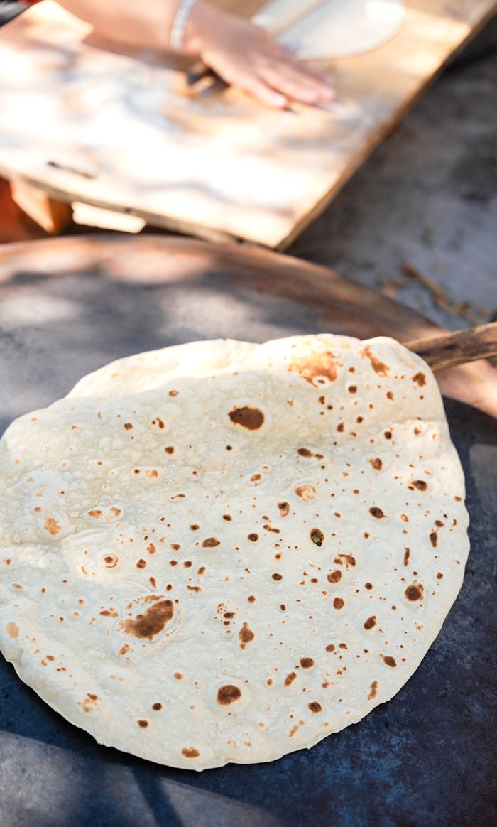 Close-up of flatbread cooking on an outdoor griddle with a baker in the background.
