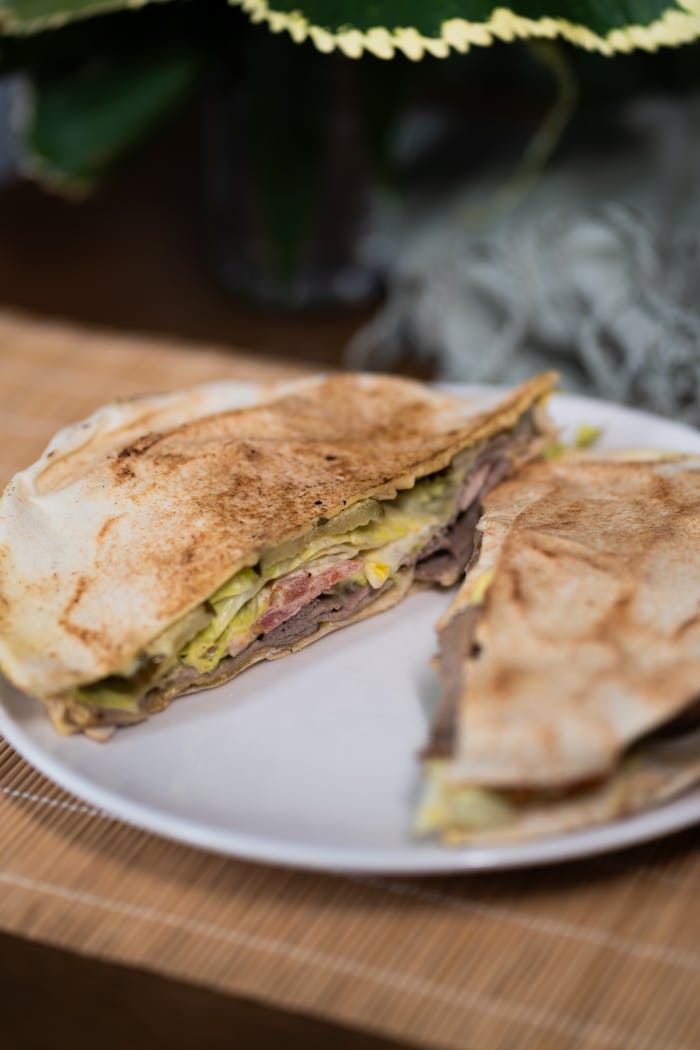 Appetizing folded sandwich with meat, cheese, and lettuce on a white plate.